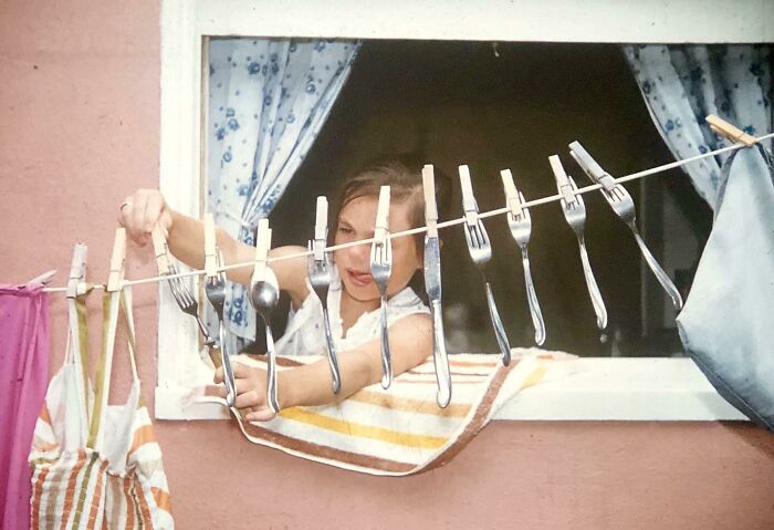Woman looking through window at cutlery hanging on clothesline, evoking America during the JFK era.
