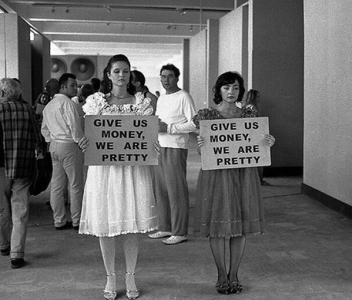 Women holding signs at a public event during the JFK years, symbolizing social dynamics of the era.