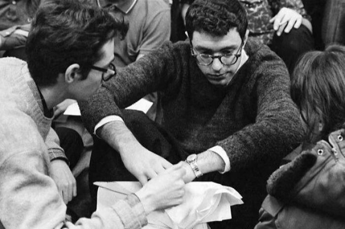 Young people in sweaters and glasses, gathered and engaged, reflecting American culture during the JFK era.