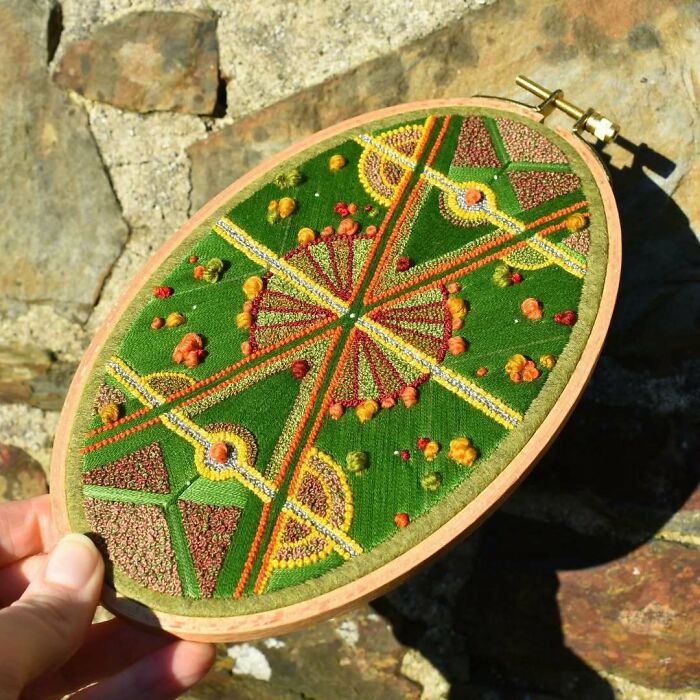 Landscape embroidery with intricate green, red, and yellow patterns in an oval hoop, showcasing artistry by Victoria Rose Richards.