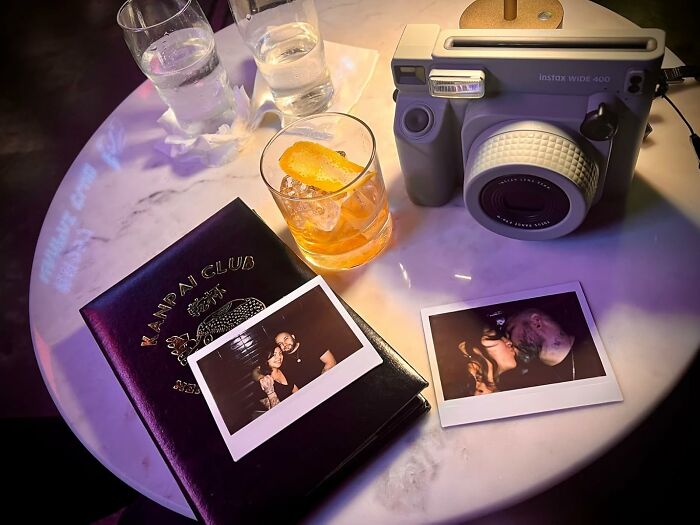 Instant camera, cocktails, polaroids, and notebook on a table, symbolizing a digital detox experience.