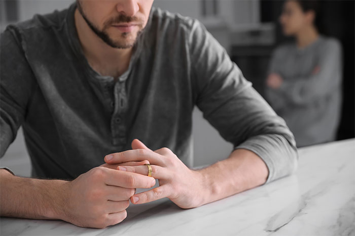 Man contemplating at table, wearing a ring, with blurred woman in the background, related to surprising daughter with tapes. Man contemplating at table, wearing a ring, with blurred woman in the background, related to surprising daughter with tapes.