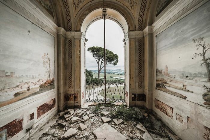 Abandoned place with c*****d floor, ornate walls, and a scenic view through an archway.
