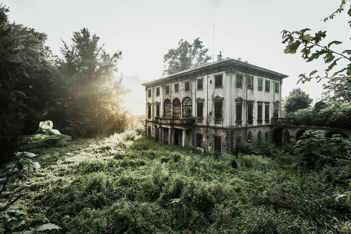 Abandoned mansion surrounded by overgrown vegetation.