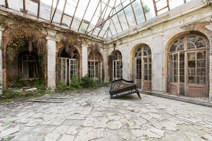 Abandoned place with dilapidated piano in a decaying glass-roofed atrium.