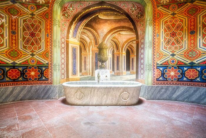 Luxurious abandoned place with ornate wall designs and a central stone bathtub.
