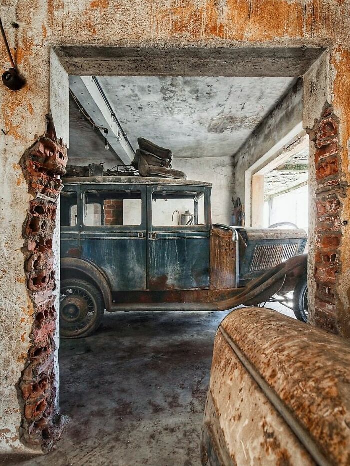 Rusty vintage car in an abandoned, decaying garage with exposed brick walls.