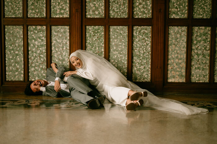 Bride and groom in joyful moment, lying on floor in elegant attire, showcasing one of the best engagement photos of 2025.