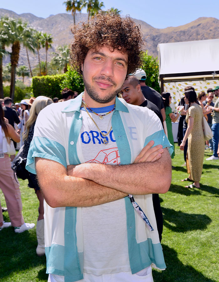 Man with curly hair in a casual outdoor event, wearing a green and white shirt, arms crossed, looking at the camera. Man with curly hair in a casual outdoor event, wearing a green and white shirt, arms crossed, looking at the camera.