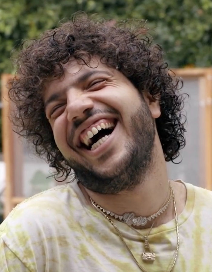 Person with curly hair and necklace, smiling broadly outdoors; topic on shower habit raises fan reactions. Person with curly hair and necklace, smiling broadly outdoors; topic on shower habit raises fan reactions.