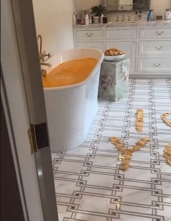 Bathtub filled with an orange liquid, snacks on a stand, and chips arranged on floor—scene linked to Benny Blanco's shower habit. Bathtub filled with an orange liquid, snacks on a stand, and chips arranged on floor—scene linked to Benny Blanco's shower habit.