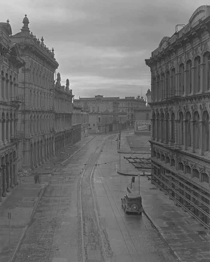 Vintage street scene showcasing old American architecture with ornate building facades and a lone car on a damp road.