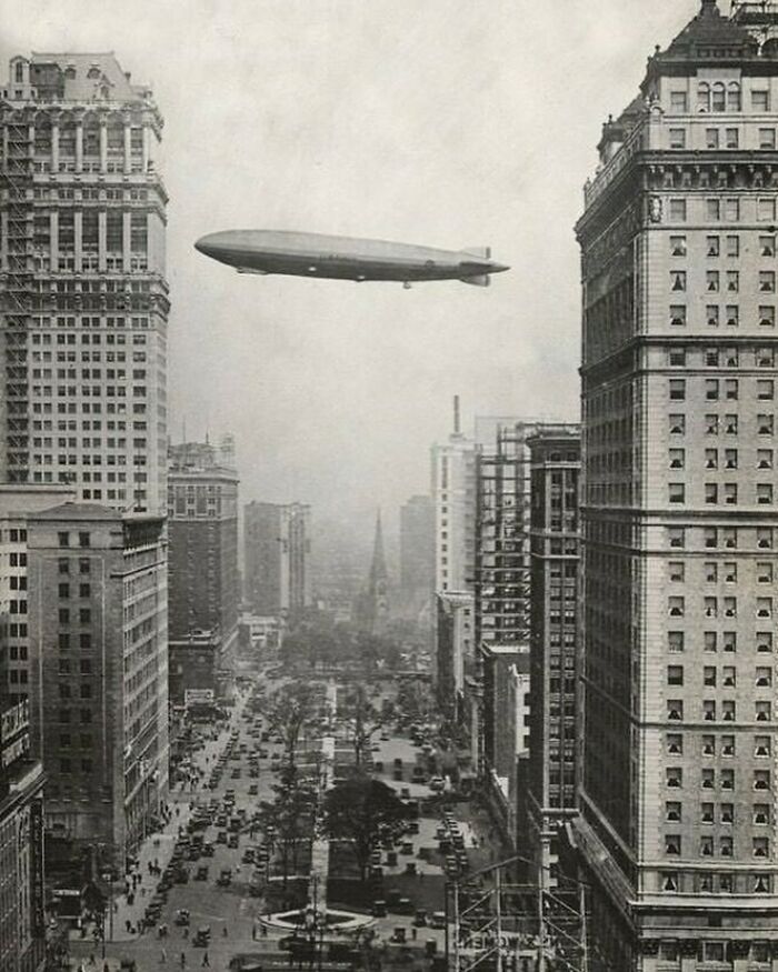 Zeppelin flying over early 20th-century skyscrapers, showcasing old American architecture.