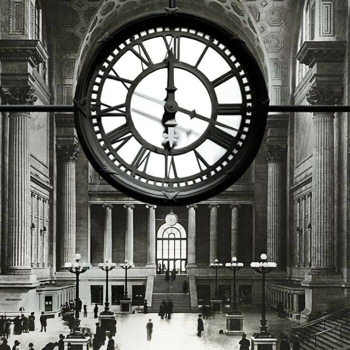 Clock in grand hall of historic American architecture, featuring classical columns and arched windows.