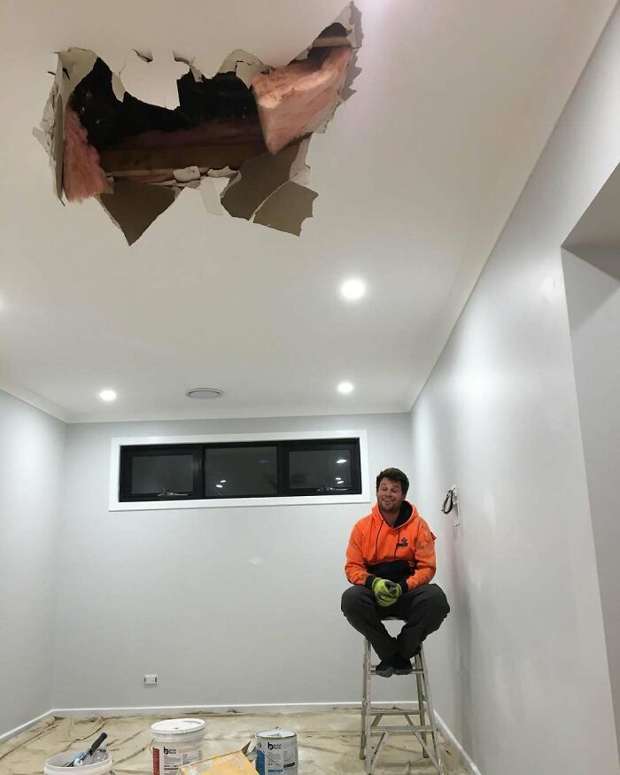 Man in orange hoodie on ladder below ceiling damage, illustrating poor decisions in house repair.