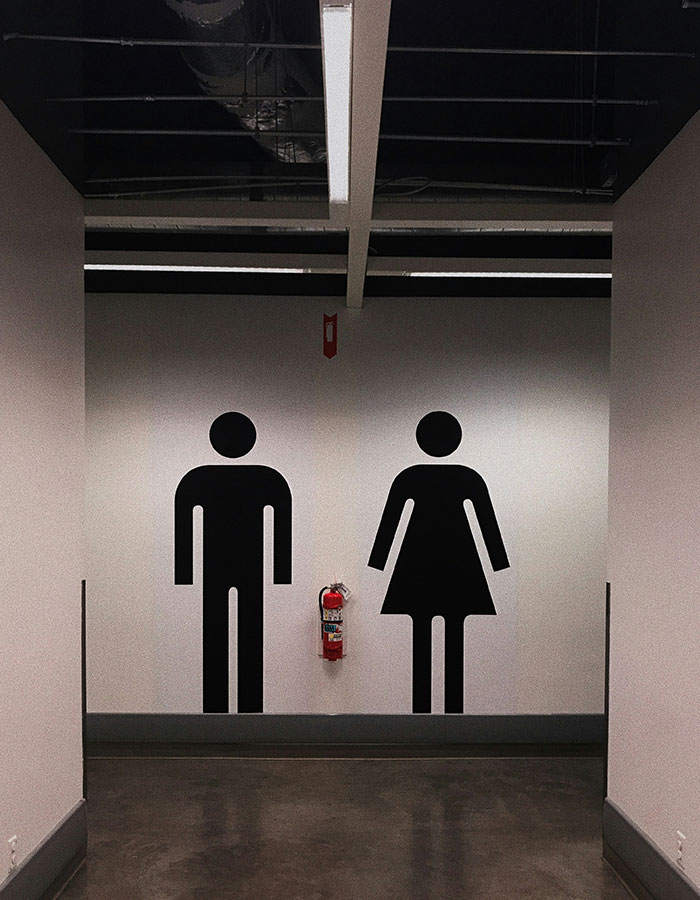 Restroom sign with male and female icons on a wall above a fire extinguisher. Restroom sign with male and female icons on a wall above a fire extinguisher.