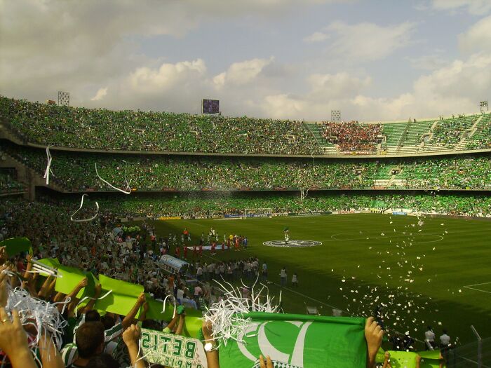 Soccer stadium filled with fans waving green flags and celebrating, capturing the spirit of cathedrals of soccer.