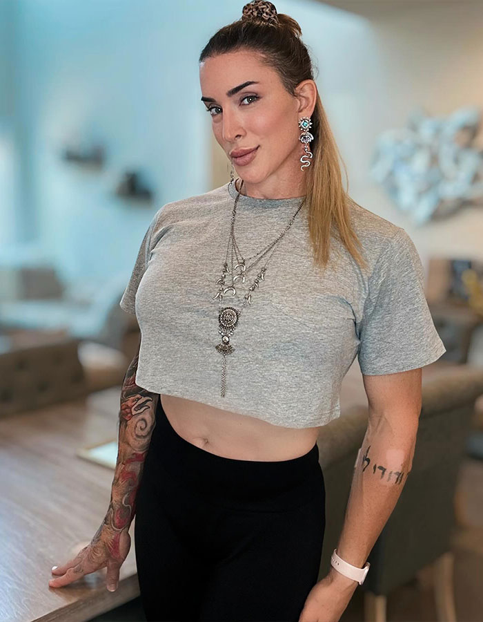 Former WWE star in a grey crop top and earrings, showing her transition journey with confidence in a bright room. Former WWE star in a grey crop top and earrings, showing her transition journey with confidence in a bright room.