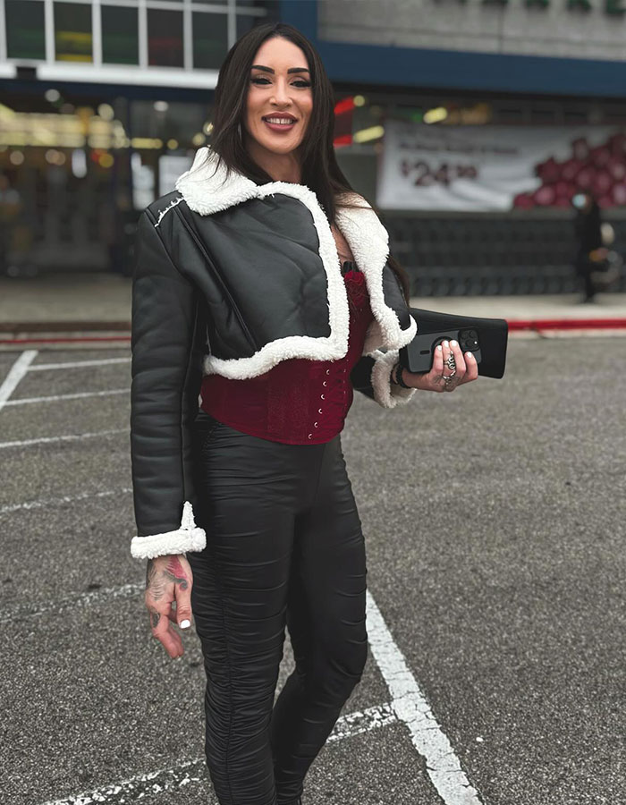 Former WWE star in a black jacket and burgundy corset, smiling in a parking lot, showcasing transition. Former WWE star in a black jacket and burgundy corset, smiling in a parking lot, showcasing transition.