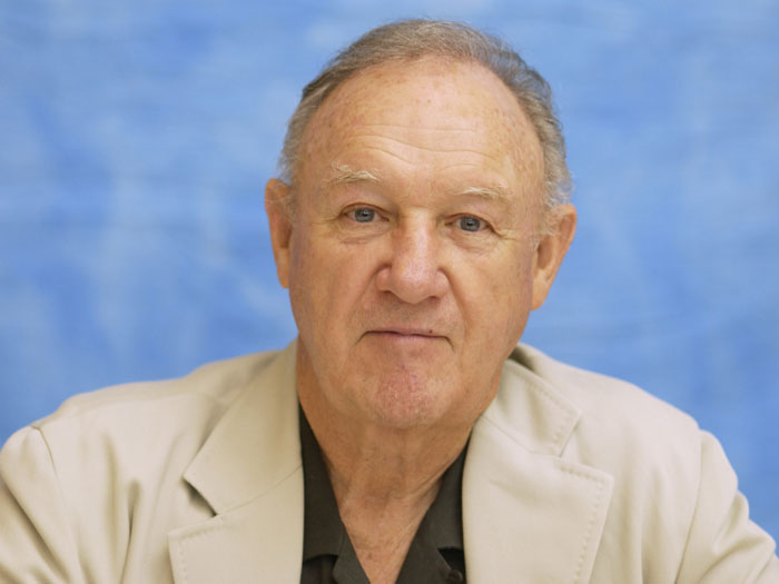 A person with a serious expression, wearing a beige jacket, against a blue background. A person with a serious expression, wearing a beige jacket, against a blue background.