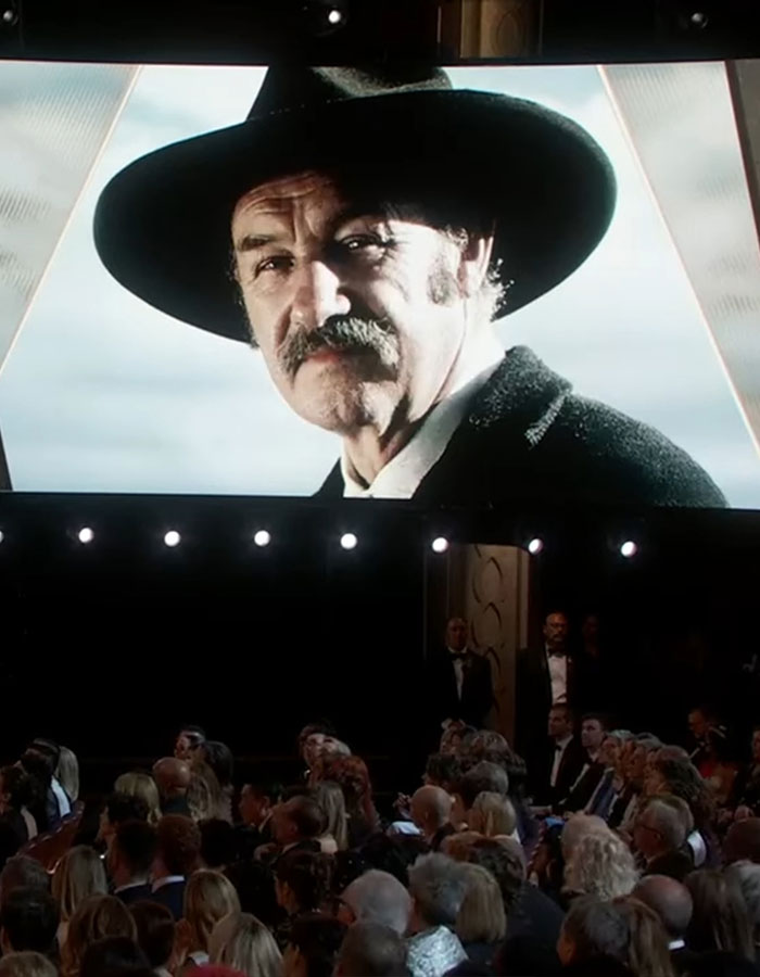 A large screen displays an image of a man in a cowboy hat at an event, with an audience seated below. A large screen displays an image of a man in a cowboy hat at an event, with an audience seated below.