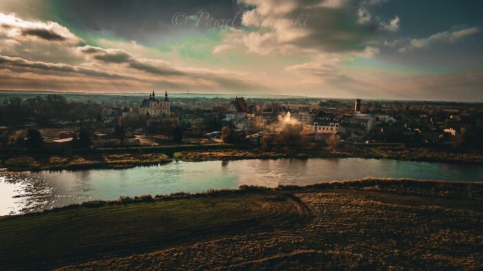 Aerial view of a city with a river in the foreground, showcasing the landscape and architecture under a cloudy sky.