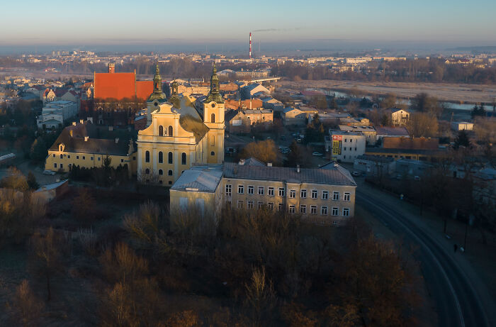 Aerial view of a city with historic buildings, roads, and distant urban landscape at sunrise.