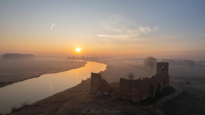 Aerial view of a cityscape with ruins, river, and sunrise in the distance.