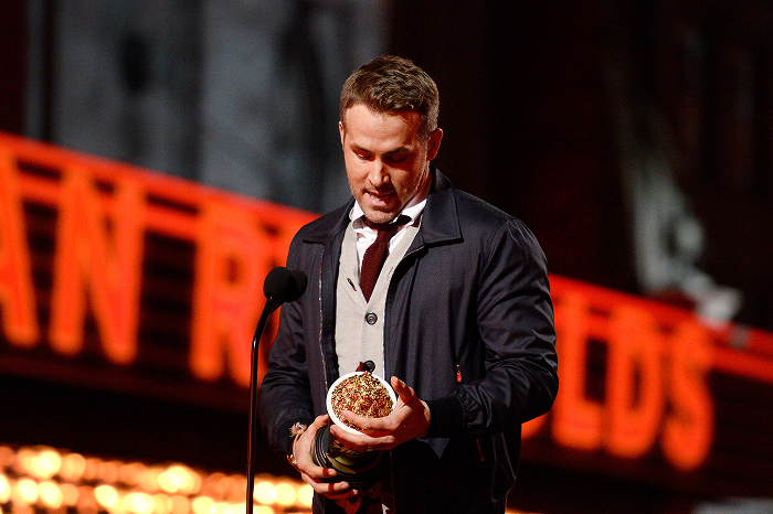 Ryan Reynolds holding an award on stage, wearing a suit, under bright lights, reflecting on business success and net worth achievements. Ryan Reynolds holding an award on stage, wearing a suit, under bright lights, reflecting on business success and net worth achievements.