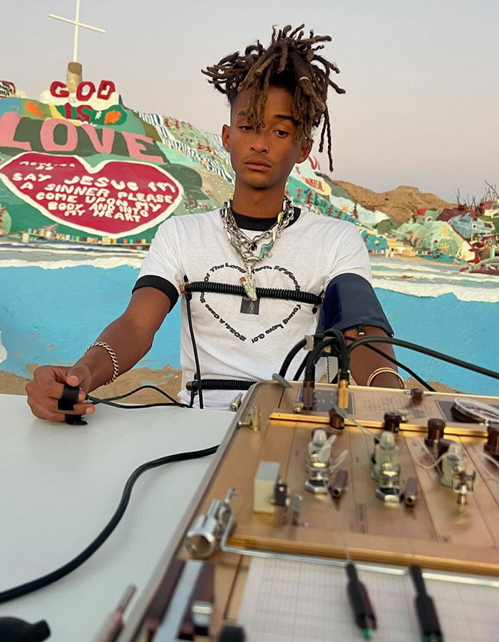 Person with unusual style at colorful location, seated with equipment. Sparks concern for 'strange' appearance. Person with unusual style at colorful location, seated with equipment. Sparks concern for 'strange' appearance.