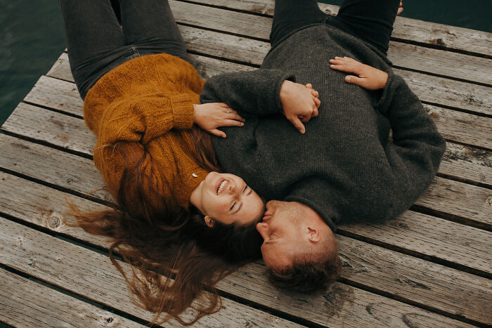 Couple lying on a wooden dock, smiling, in one of the best engagement photos of 2025.