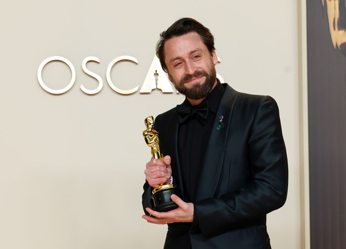 Man in a black suit holding an Oscar trophy, smiling at the Oscars 2025 event. Man in a black suit holding an Oscar trophy, smiling at the Oscars 2025 event.