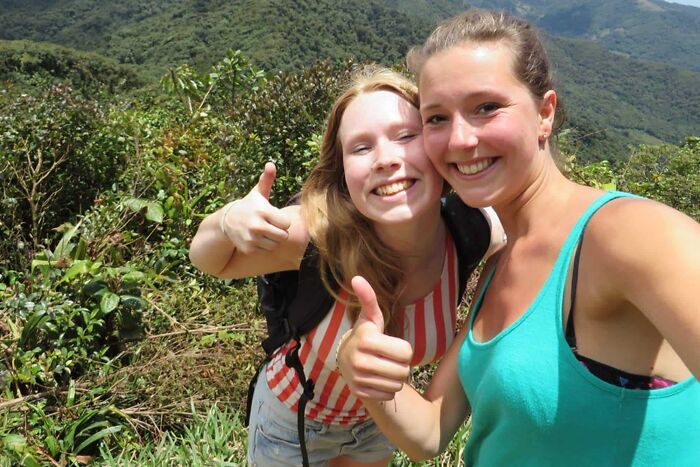 Two smiling women giving thumbs up in a lush, green mountainous area; creepy photo with a dark history. Two smiling women giving thumbs up in a lush, green mountainous area; creepy photo with a dark history.