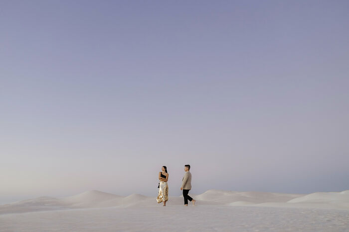 Couple walking on white sand dunes at sunset, showcasing one of the best engagement photos of 2025.