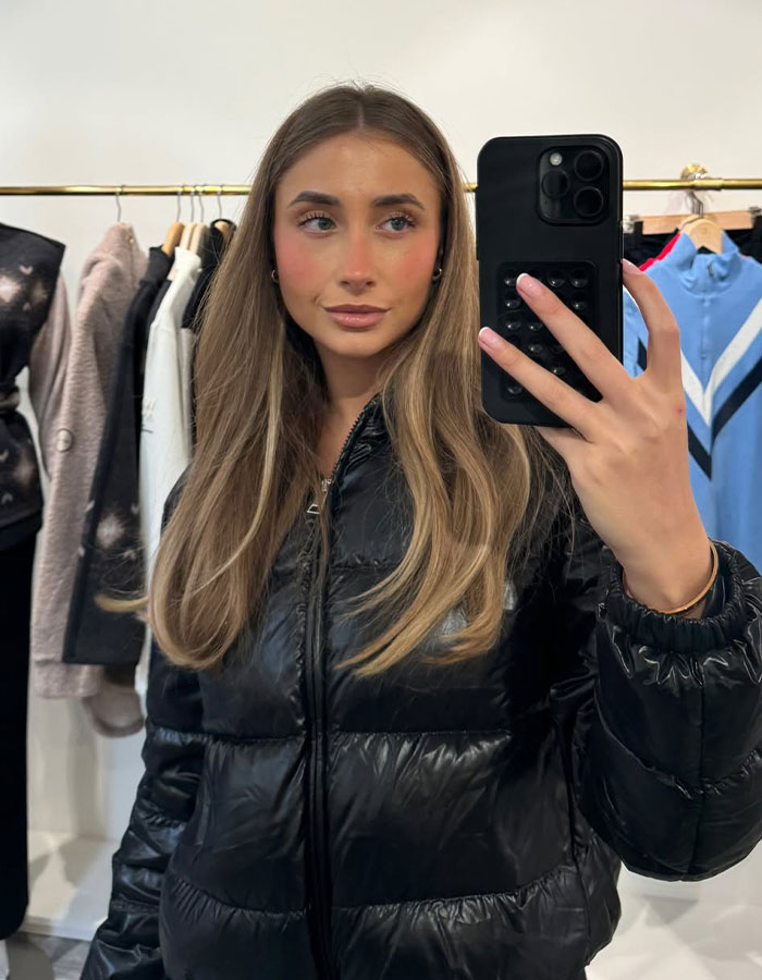 Woman in black puffer jacket taking a mirror selfie in a clothing store. Woman in black puffer jacket taking a mirror selfie in a clothing store.