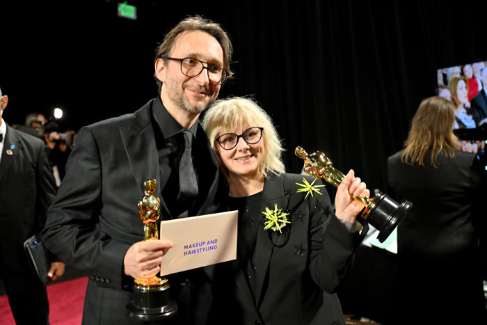 Winners at the Oscars 2025 holding awards and an envelope for Makeup and Hairstyling, smiling on stage. Winners at the Oscars 2025 holding awards and an envelope for Makeup and Hairstyling, smiling on stage.