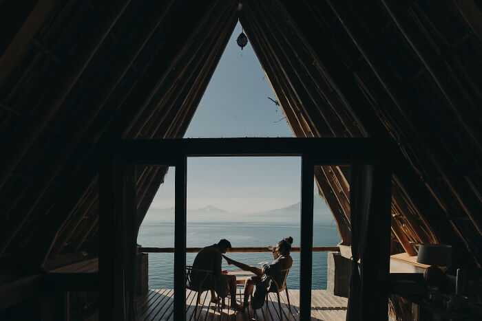 Couple sitting inside an A-frame cabin overlooking the ocean, capturing one of the best engagement photos of 2025.