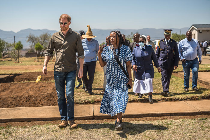 Harry and charity boss walking outdoors, surrounded by a group, in a formal setting. Harry and charity boss walking outdoors, surrounded by a group, in a formal setting.