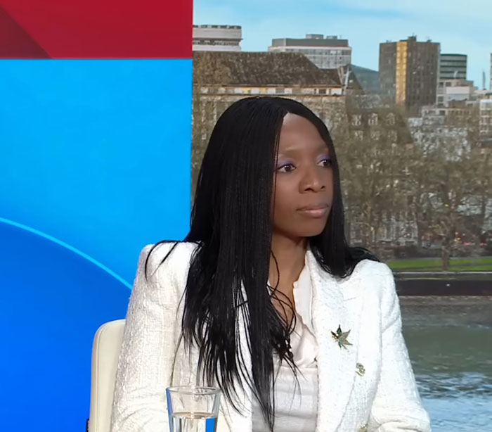 A woman in a white jacket on a TV set discussing Harry's charity and Meghan. A woman in a white jacket on a TV set discussing Harry's charity and Meghan.