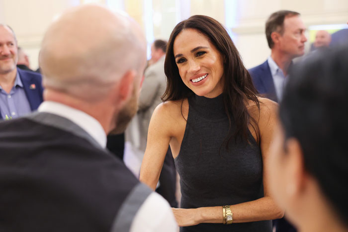 Person in a sleeveless dress smiling in conversation at a social event, highlighting a friendly interaction. Person in a sleeveless dress smiling in conversation at a social event, highlighting a friendly interaction.
