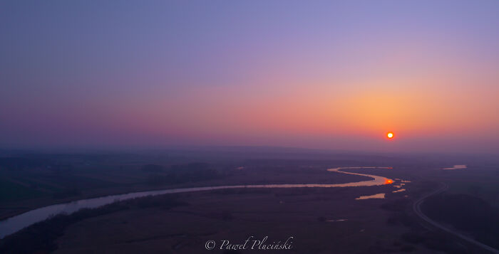 Aerial view of a cityscape at sunset with winding river reflecting the sun.