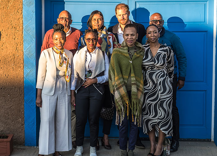 A group of people standing together in front of a blue door, related to Prince Harry's charity. A group of people standing together in front of a blue door, related to Prince Harry's charity.