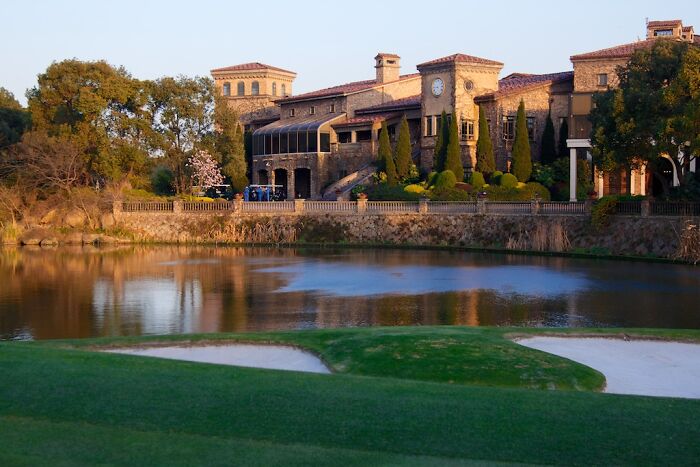 Breathtaking golf course with a scenic view of a clubhouse by the water, surrounded by lush greenery.