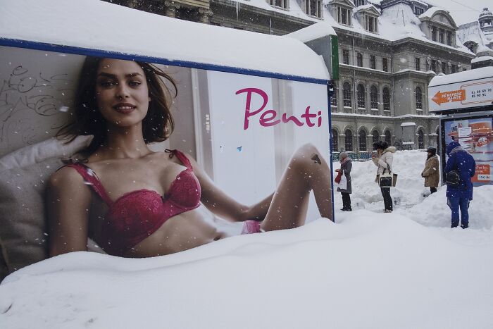 Street photo shows a winter scene with a billboard partially covered in snow, creating a comedic illusion.