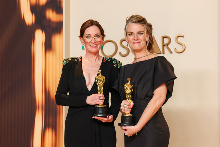 Two women holding Oscar trophies at the 2025 Oscars ceremony, standing in front of a backdrop with the word "Oscars. Two women holding Oscar trophies at the 2025 Oscars ceremony, standing in front of a backdrop with the word "Oscars.