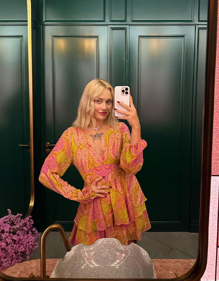 Blonde woman in a colorful dress taking a mirror selfie in a green room. Blonde woman in a colorful dress taking a mirror selfie in a green room.
