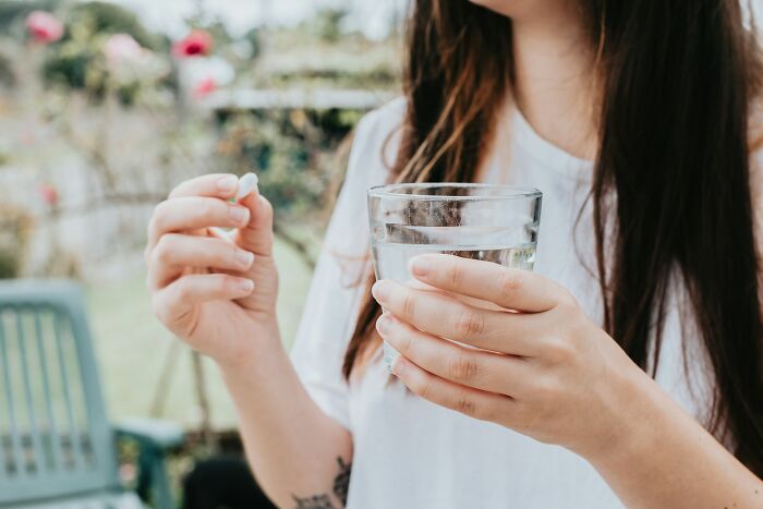 A woman in a garden holding a pill and a glass of water, symbolizing common job misconceptions.
