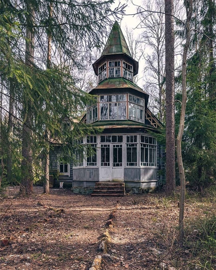 Abandoned wooden house with a pointed roof surrounded by trees, showcasing its aged beauty with time.