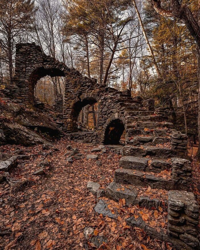 Abandoned stone ruins in a forest setting, surrounded by autumn leaves, showcasing nature's beauty over time.