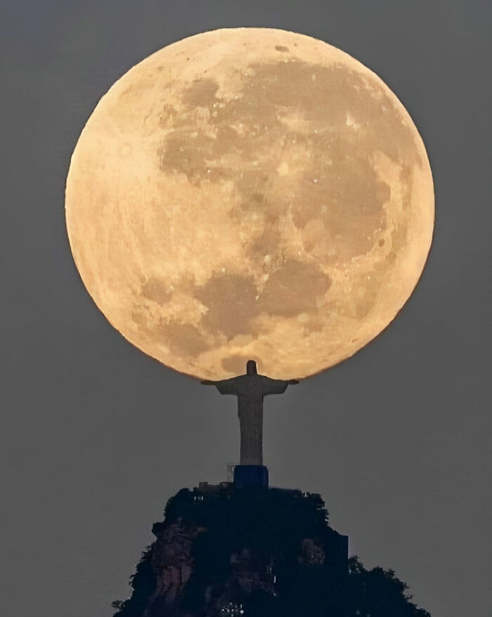 Massive full moon setting behind a silhouette statue, capturing stunning space scenery.